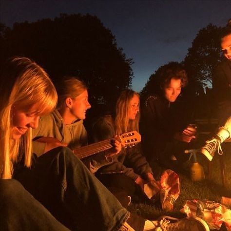 a group of young people sitting around a campfire playing guitars and singing to the music