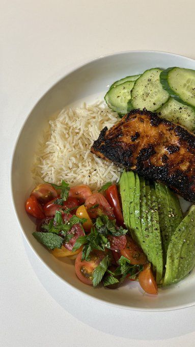 a white plate topped with rice, cucumber slices and other food on top of it