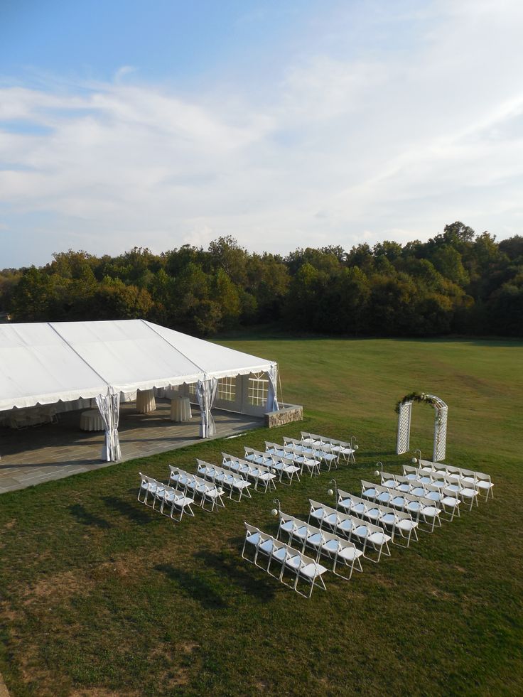 a large white tent set up for a wedding with rows of chairs in the grass