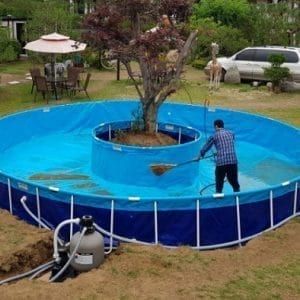 a man is standing in the middle of an above ground swimming pool with a tree