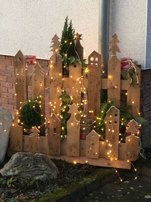 a wooden fence decorated with christmas lights and potted plants in front of a house