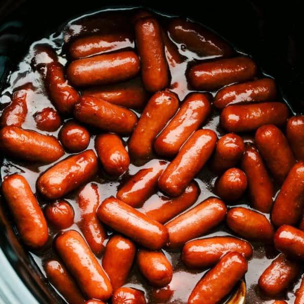 a crock pot filled with cooked hotdogs and ketchup on the side