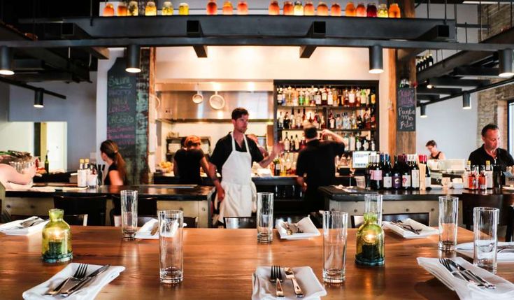 people are sitting at the bar in a restaurant with empty glasses on the table, and two bartenders behind them