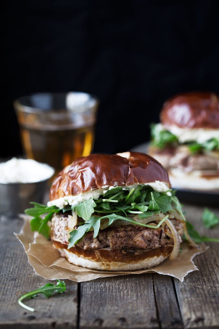 two burgers with meat, lettuce and cheese on wooden table next to glass of beer