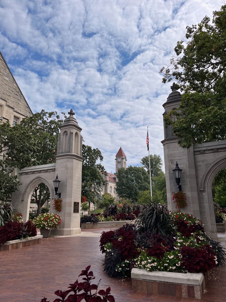 a clock tower in the middle of a courtyard with flowers and trees on either side