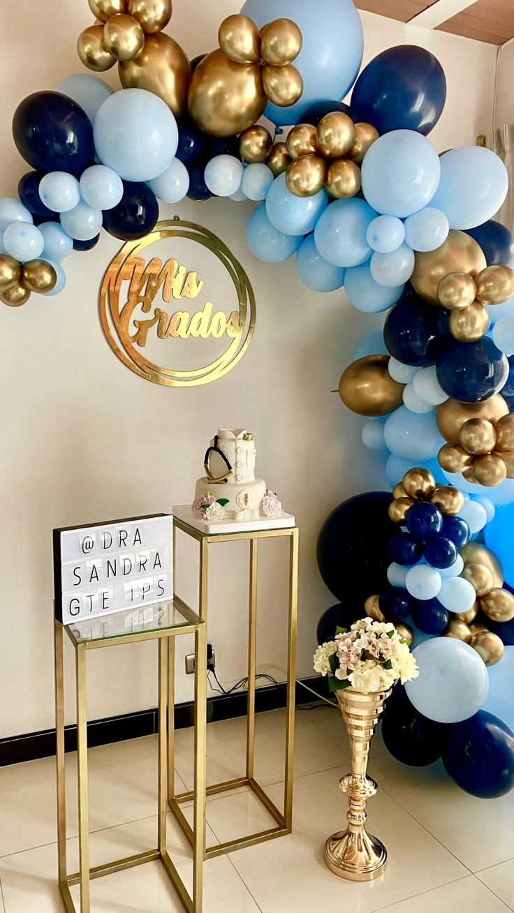 an arch made out of balloons and gold stands in front of a table with a cake on it