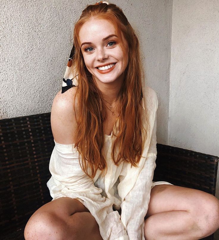 a young woman sitting on top of a wooden bench next to a white brick wall