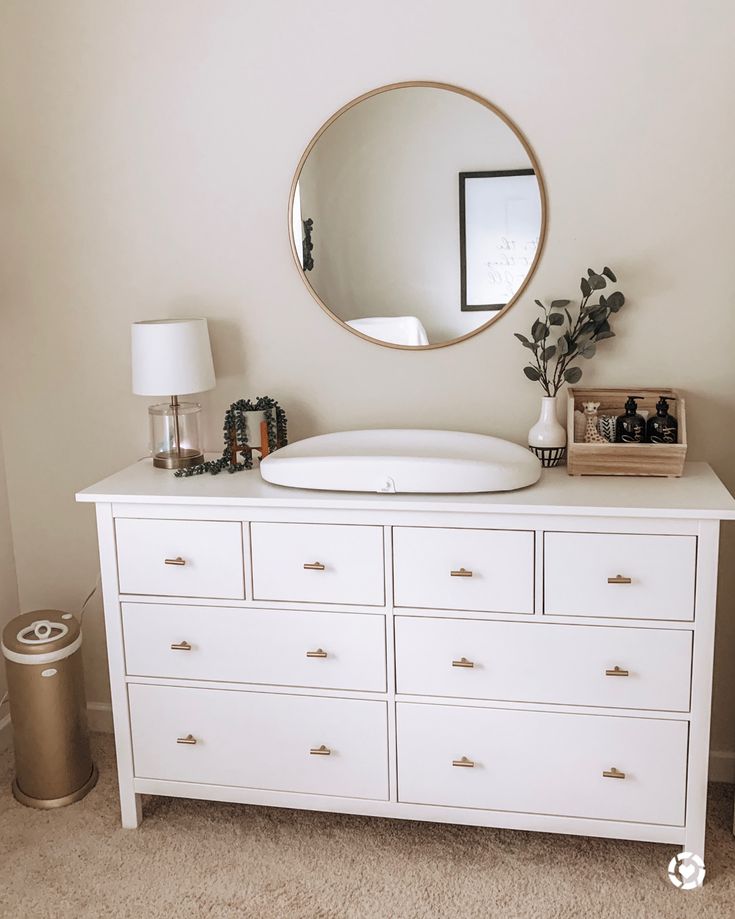 a white dresser with a round mirror above it