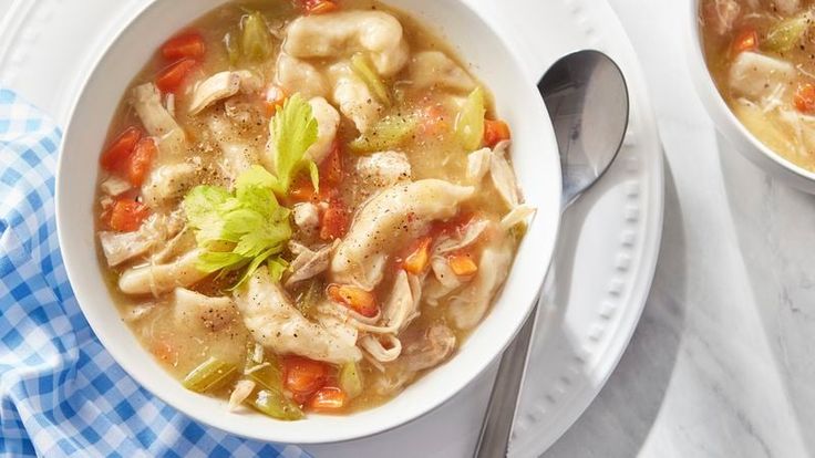 two bowls of chicken noodle soup on a white and blue checkered table cloth