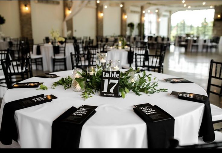 the table is set with black and white linens, greenery and candle holders