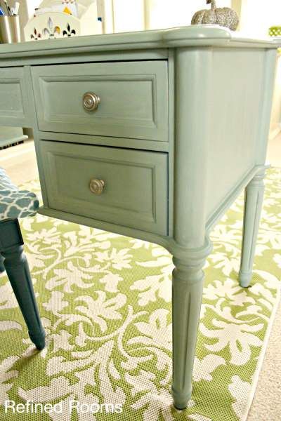 a green table with two drawers and a blue chair next to it on a rug