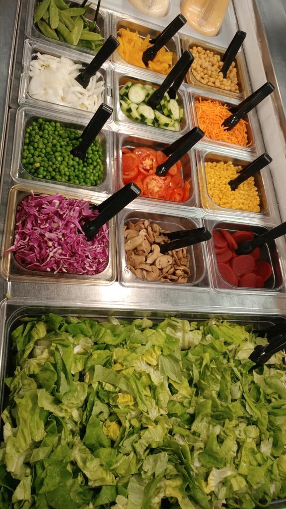 several trays filled with different types of vegetables and salad dressing on top of each other