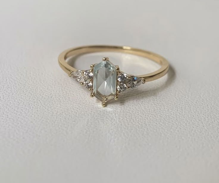 a gold ring with an aqua blue stone and three white diamonds on the side, sitting on a plain surface