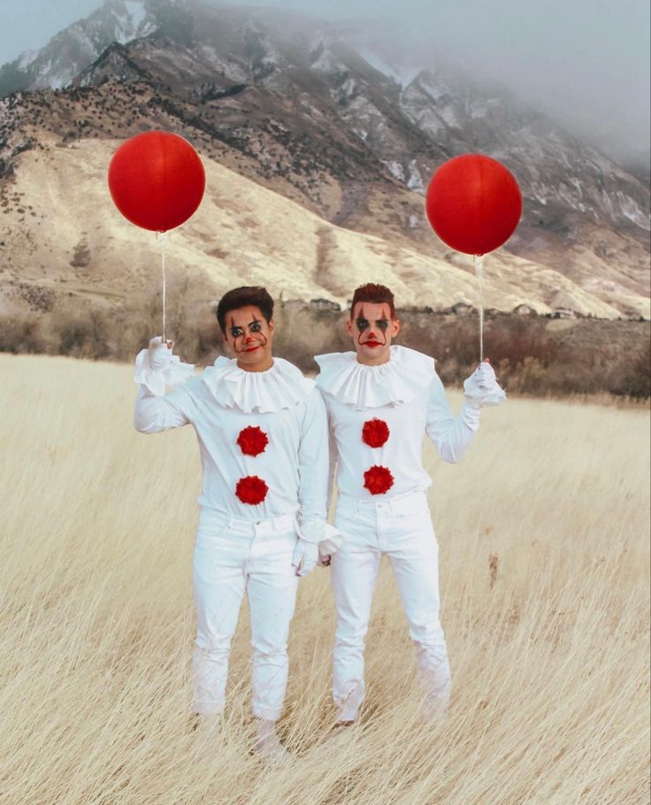 two men in white costumes holding red balloons with mountains in the background