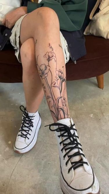 a woman sitting on top of a couch with her legs crossed and flowers tattooed on the leg