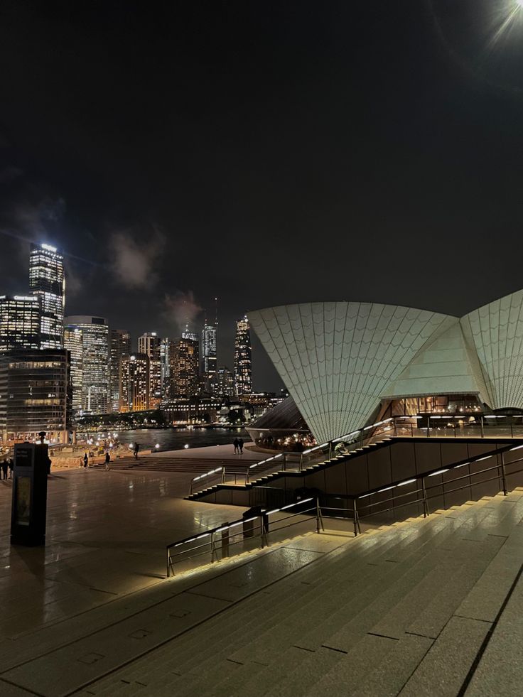 the sydney opera house is lit up at night with city lights in the back ground