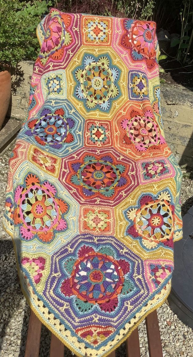 a colorful crocheted blanket sitting on top of a wooden bench next to plants