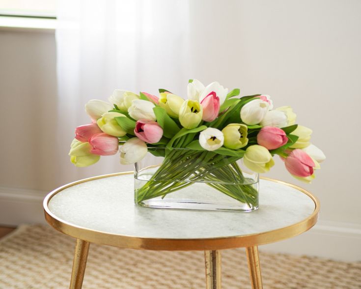 a glass vase filled with pink and white tulips on top of a table