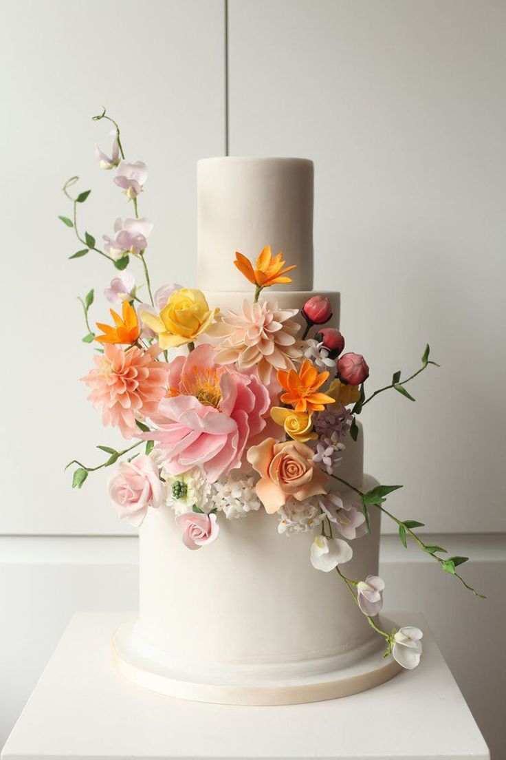 a three tiered white wedding cake with flowers on the top and bottom, sitting on a pedestal