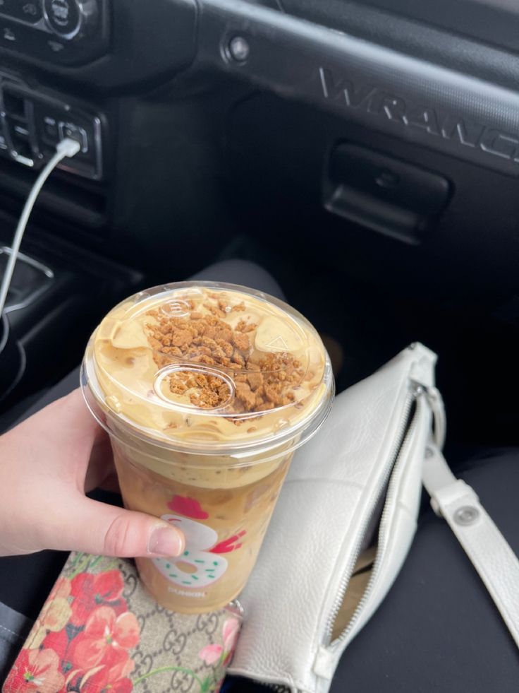 a hand holding a cup of coffee in front of a car steering wheel and dashboard