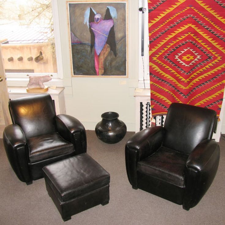 two leather chairs and a foot stool in front of a window with an abstract painting on the wall