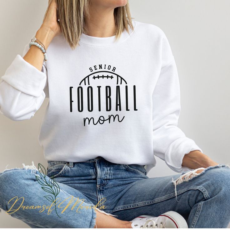 a woman sitting on the floor wearing a sweatshirt that says football mom