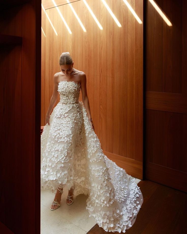 a woman in a white wedding dress standing by a wooden wall