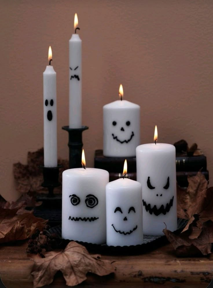 halloween candles with faces drawn on them are sitting in front of leaves and a candle holder