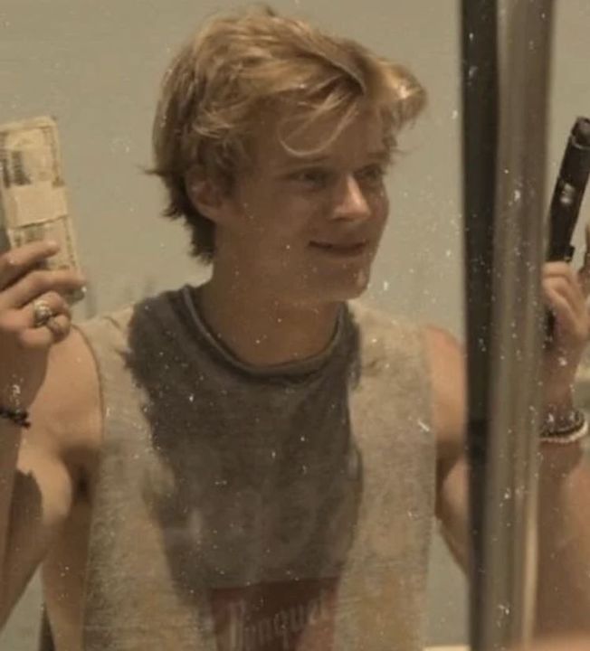 a young man holding two cell phones in front of a mirror