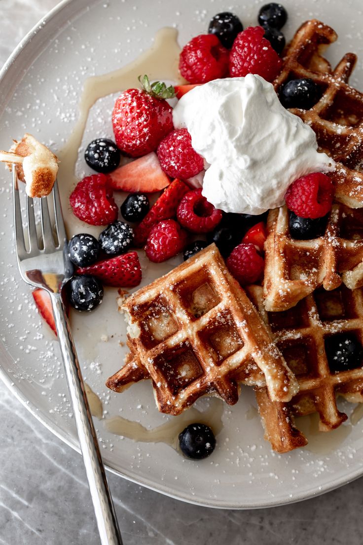 waffles, berries and whipped cream on a white plate with a fork next to it