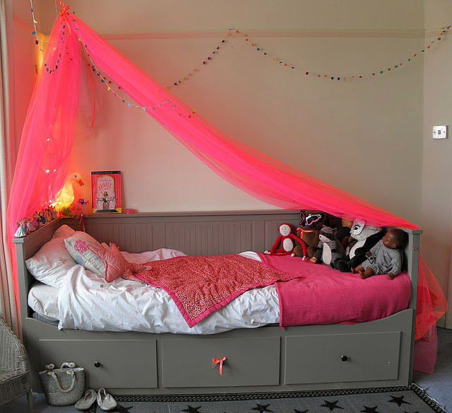 a pink canopy over a bed in a room with toys on the floor and lights above it