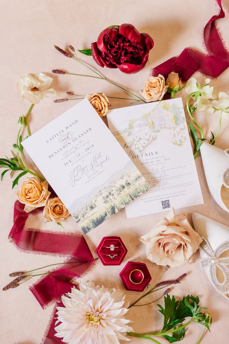 A flat lay of wedding invitations surrounded by blush roses, deep red peonies, a large pink dahlia, and wedding rings in red velvet boxes, beautifully arranged on a soft pink background. Wedding Invitation Flat Lay, Invitation Flat Lay, Pippin Hill Wedding, Pink Dahlias, Hill Wedding, Roses Red, Elegant Wedding Invitation, Charlottesville Virginia, Wine Country Wedding