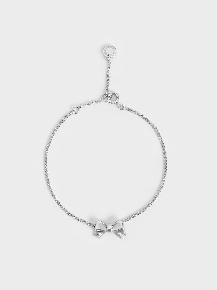 Our Paige bracelet is also available in a stunning silver finish. With its classic ribbon charm, this delicate piece is ideal for fashion lovers who want to embrace the coquette trend in an understated manner. Wear yours layered with other silver bracelets for a stylishly stacked look. Alternatively, style it with our matching Paige necklace and stud earrings for a complete set and polished look. Chic Silver Chain Bracelet With Adjustable Chain, Chic Silver Bracelets For Party, Chic Silver Chain Bracelet For Party, Minimalist Party Jewelry With Bow, Adjustable White Gold Chain Bracelet, Chic Metal Jewelry With Bow Detail, Chic Ribbon Jewelry As A Gift, Chic Jewelry With Ribbon For Gift, Chic Silver Jewelry With Ribbon