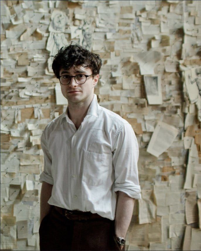 a young man standing in front of a wall covered with post - it notes and looking at the camera