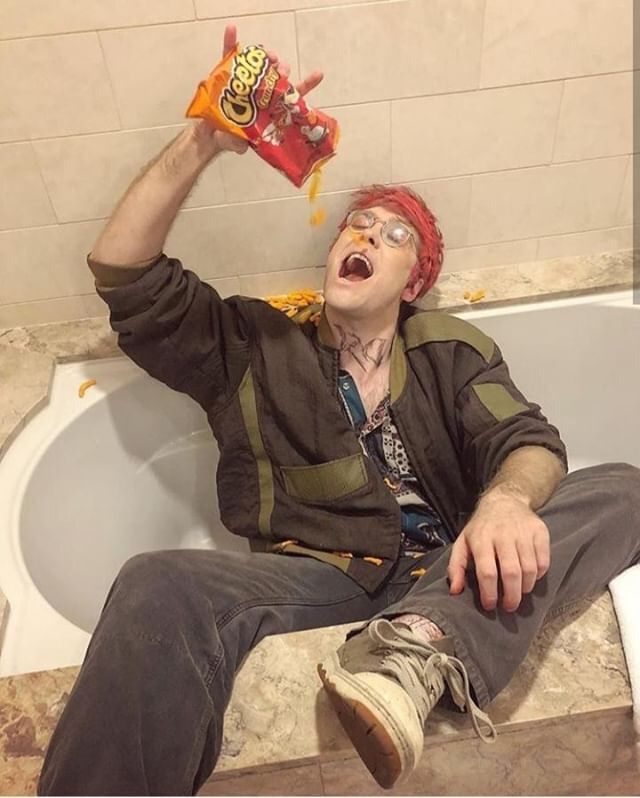 a man sitting in a bathtub with his mouth open and holding up a bag of cheetos