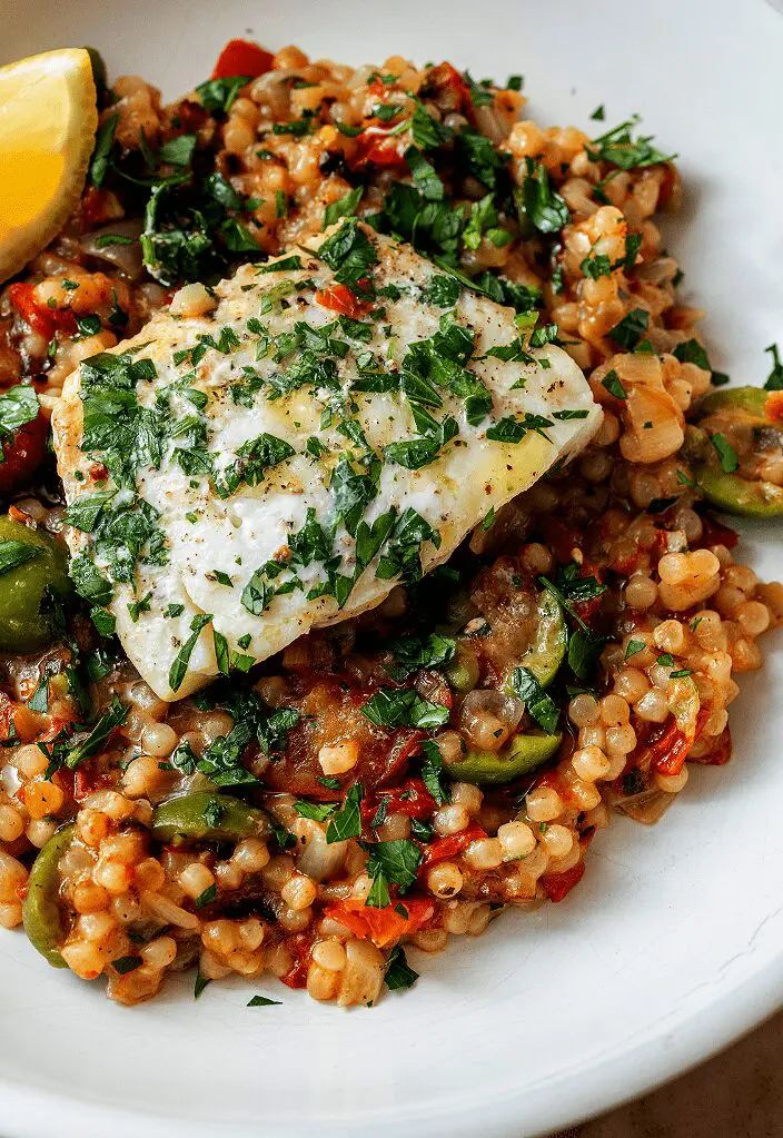 a white plate topped with fish, rice and veggies next to a lemon wedge