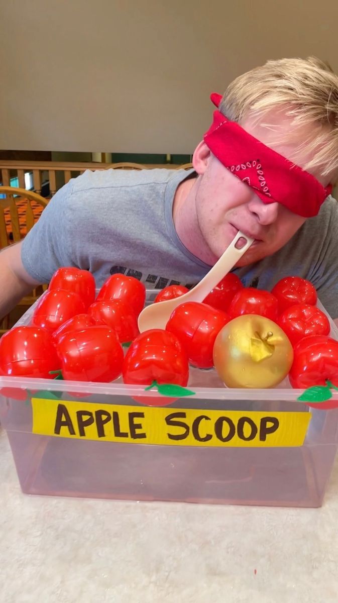 a man in blindfolded head covering eating from a container filled with tomatoes and apples