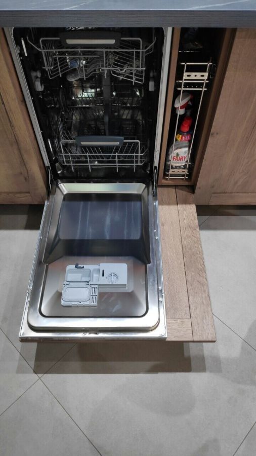 an open dishwasher in a kitchen with wooden cabinets and drawers on the floor