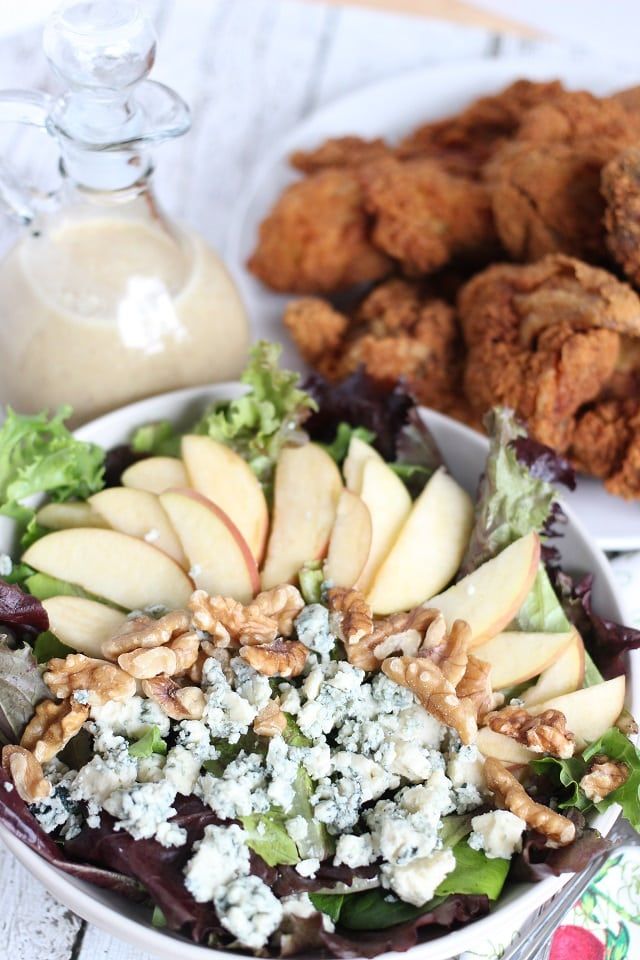 an apple, blue cheese and walnut salad in a white bowl with chicken on the side