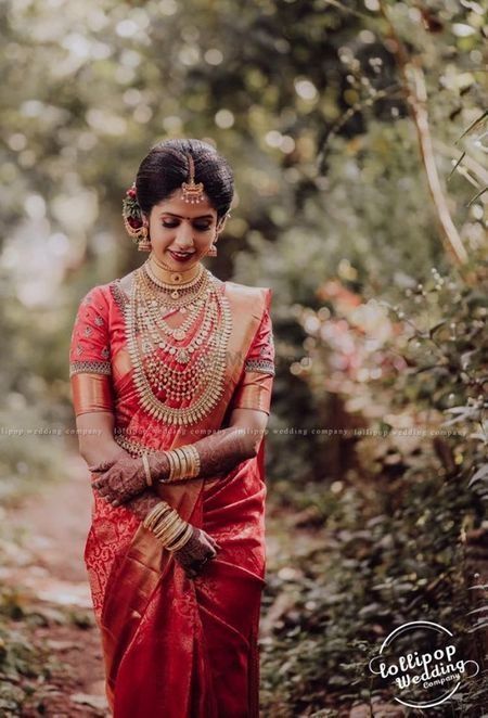 a woman in red and gold sari walking through the woods with her hands on her chest