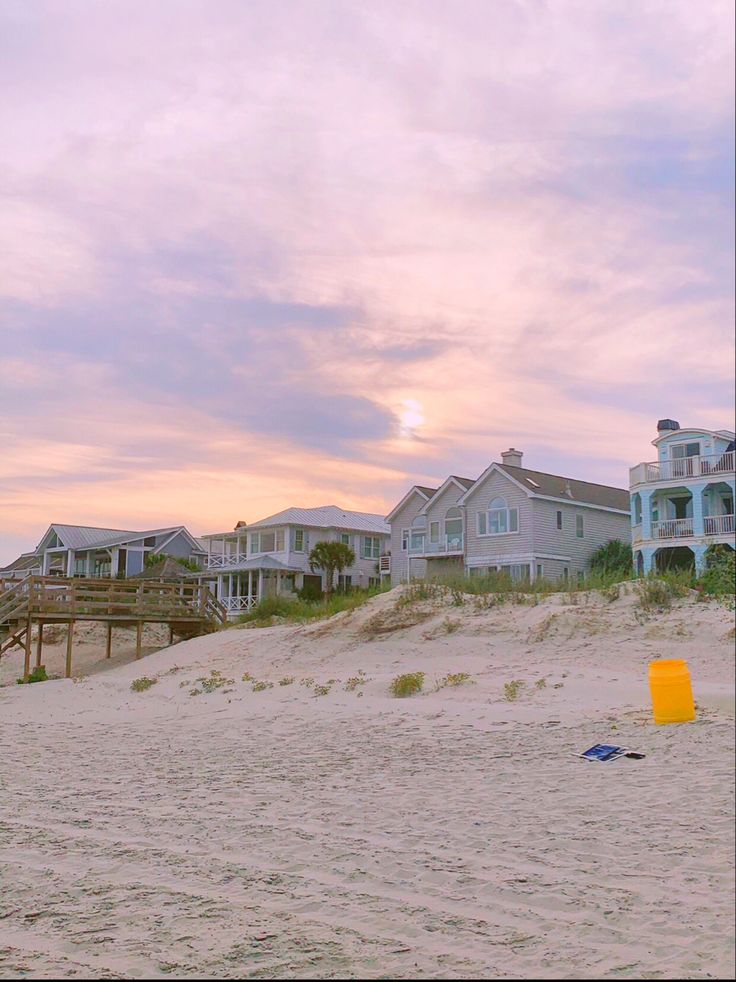 a beach with houses in the background and a frisbee on the sand at sunset