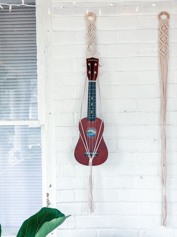 a red ukulele hanging on a white brick wall next to a green plant