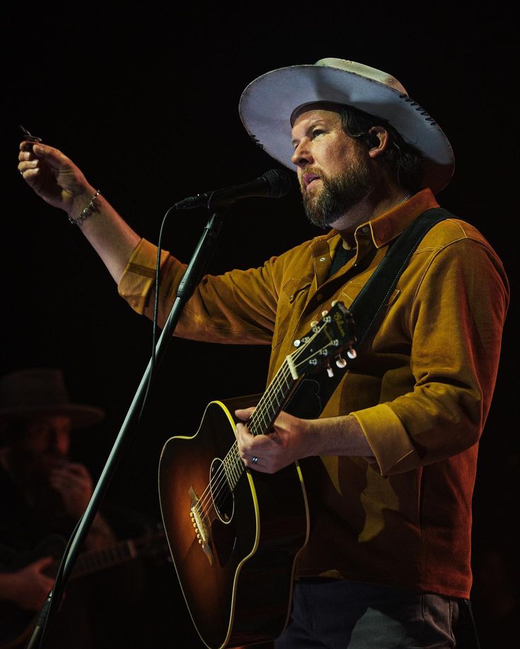 a man wearing a cowboy hat and holding a guitar in his right hand while singing into a microphone