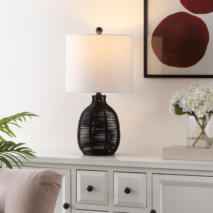 two vases with flowers sit on a white table next to a lamp and dresser