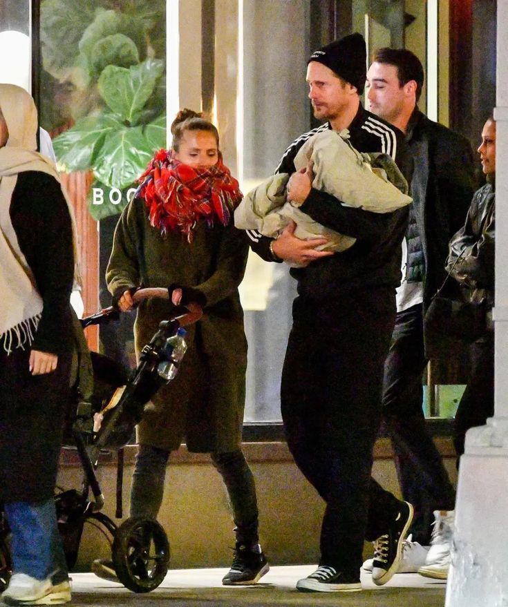 a group of people walking down the street with one holding a baby in her arms