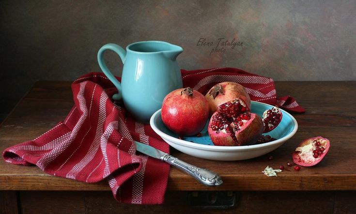 a bowl of pomegranates on a table with a pitcher and knife