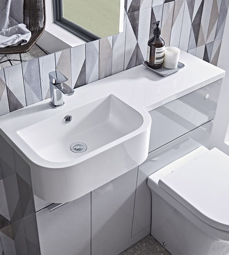 a white bathroom sink sitting next to a toilet under a mirror on a tiled wall