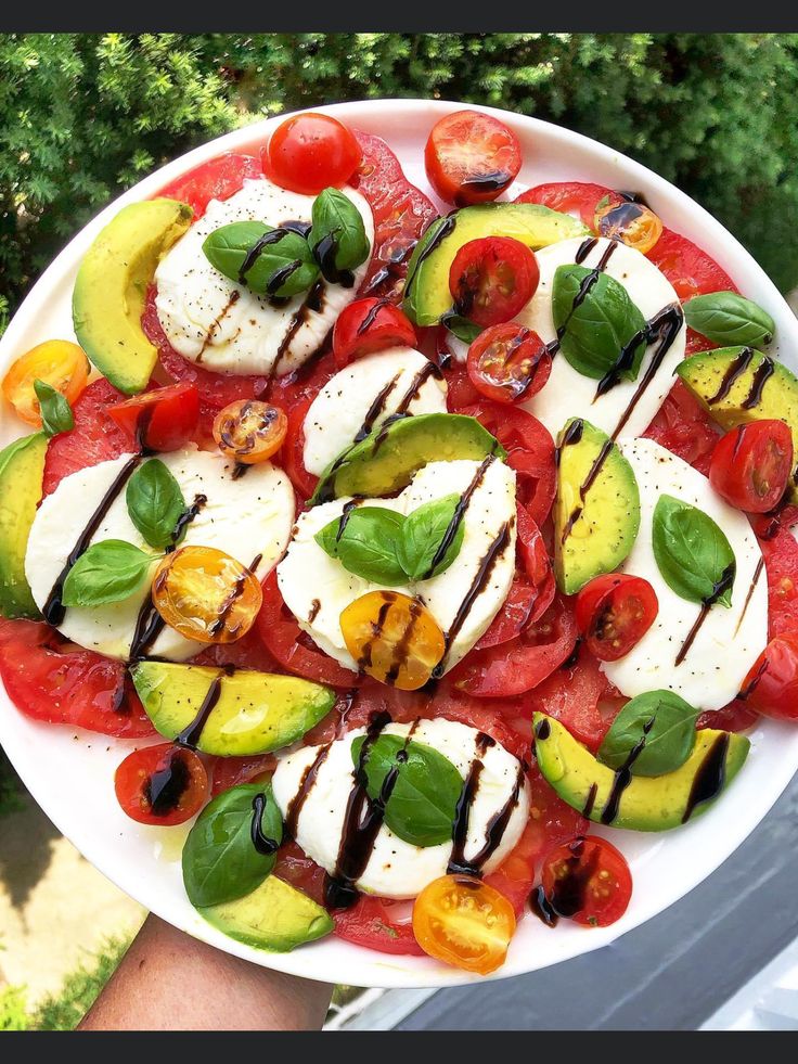 a white plate topped with sliced tomatoes, cucumbers and mozzarella