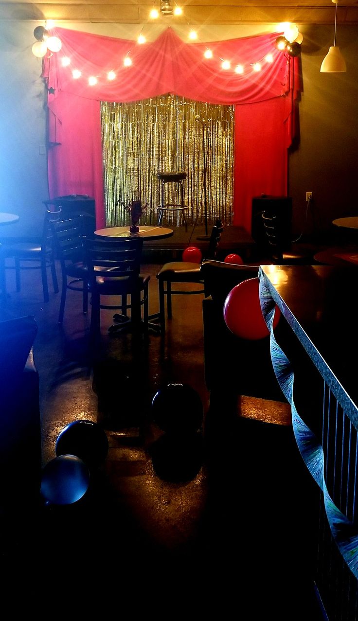 a dark room with red curtains and lights on the windowsills, black chairs and round tables