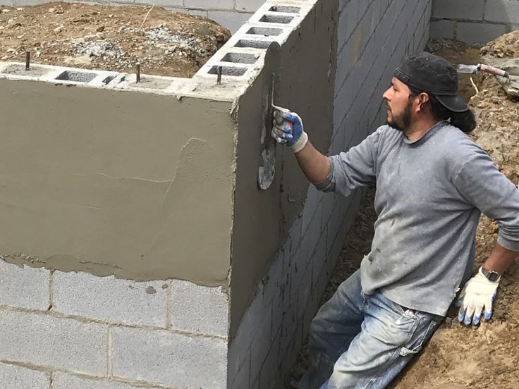 a man that is standing next to a wall with cement in his hand and another person behind him